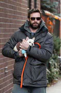 a man holding a small dog in his arms while walking down the street on a sidewalk