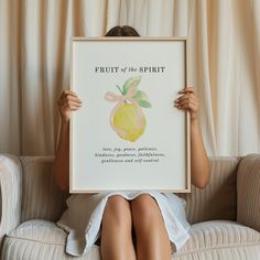 a woman sitting on a couch holding up a framed poster with the words fruit of the spirit