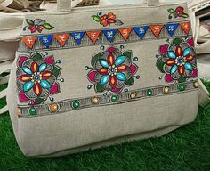 an embroidered bag sitting on top of grass next to other bags in the back ground