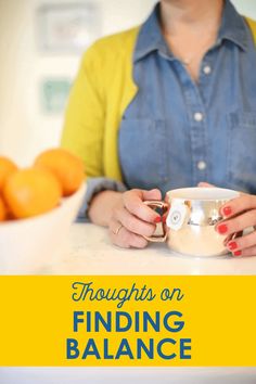 a woman is holding a coffee cup in front of some oranges on the counter