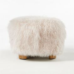 a white sheepskin footstool with wooden legs on a plain surface, in front of a white background