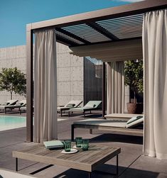 an outdoor patio area with lounge chairs and tables next to a pool in the background