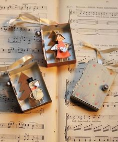 three christmas ornaments are sitting on top of sheet music and decorated with bells, snowmen, and angels