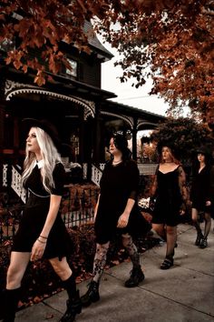 three women in black dresses are walking down the sidewalk with their hands on their hips