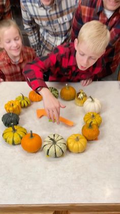 two boys and one girl are making a wreath made out of pumpkins on a table