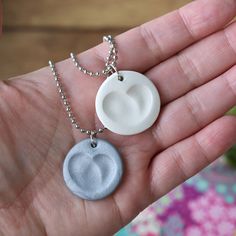 a person is holding two different pendants in their hand, one has a white disc on it