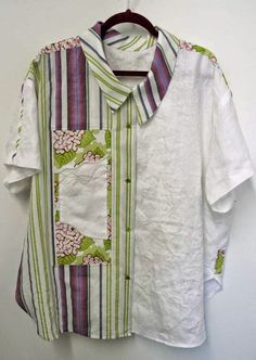 a white shirt with green and pink flowers on it hanging from a wooden hanger