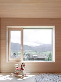 a rocking horse sits in front of a large window with mountains out the back ground