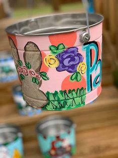 a tin can with flowers painted on it hanging from a string in front of other tin cans