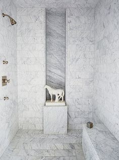 a bathroom with marble walls and flooring, including a white shower stall that has a statue of a dog on it