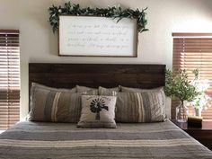 a bed with two pillows on top of it next to a wooden headboard and window blinds