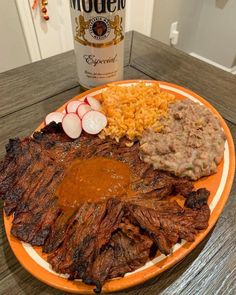 an orange plate topped with meat, rice and veggies next to a bottle of booze