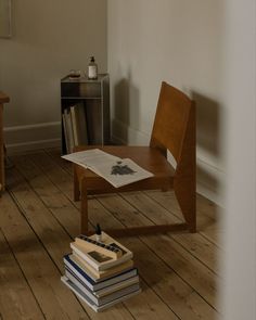 a stack of books sitting on top of a wooden floor next to a chair and table