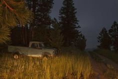 an old pick up truck parked on the side of a dirt road at night time