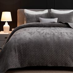 a bed with grey bedspread and white pillows in a dark colored bedroom setting