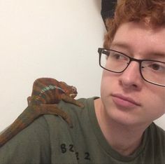 a young man with glasses and a lizard on his shoulder, looking at the camera