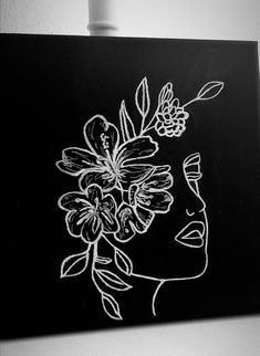 a black and white drawing of a woman's face with flowers in her hair