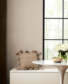 a vase with flowers sitting on top of a white table next to a large window