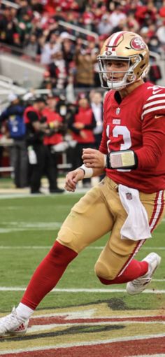 a football player running with the ball in his hand and people watching from the bleachers