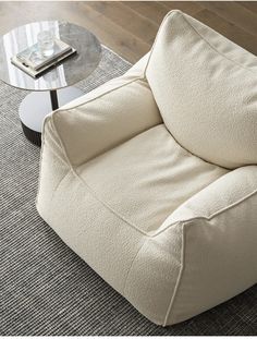 a white chair sitting on top of a rug next to a glass table with a book