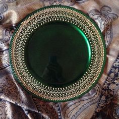 a green plate sitting on top of a blue and gold cloth covered tablecloth with an ornate design