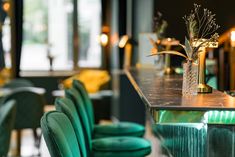 the bar is decorated with green velvet chairs and gold vases filled with greenery