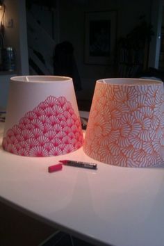 two lampshades sitting on top of a white table next to a pen and remote control