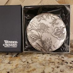 a silver plate in a black box on a marble counter top next to a brown and white tile wall