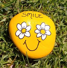 a smiley face painted on a yellow frisbee laying in the grass with flowers