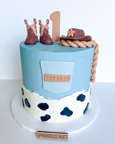 a blue and white cake decorated with cowboy boots, booties and a name tag