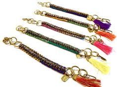 four different colored beads and tassels hanging from gold chains with keychains