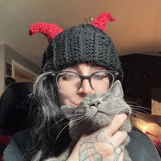 a woman holding a cat with horns on it's head while wearing a knitted hat