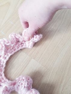 a person crocheting a piece of pink yarn on top of a wooden floor