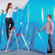 a woman standing on top of a ladder next to a man in front of a blue backdrop