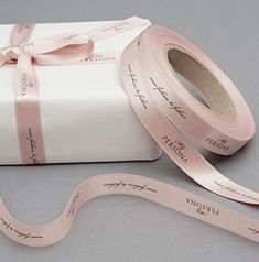 a roll of pink satin ribbon next to a white present box with writing on it