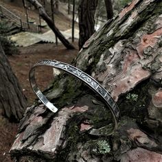 a silver bracelet sitting on top of a tree trunk in the middle of a forest