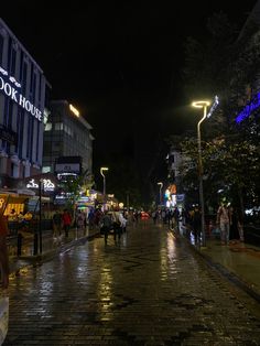 people walking down the street at night with lights on and buildings in the back ground