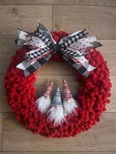 a red wreath with two gnomes on it and some white pom poms