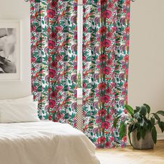 a white bed sitting next to a window covered in pink and green curtains with flowers on them