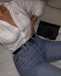 a woman wearing jeans and a white shirt is sitting on a couch with her hand in her pocket