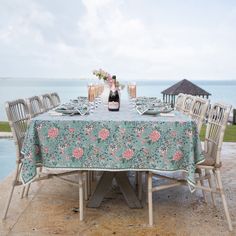 the table is set with wine and flowers on it, along with chairs that are facing the water