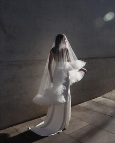 a woman in a white wedding dress and veil standing on the sidewalk with her back to the camera