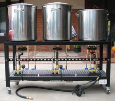 three stainless steel pots sitting on top of a metal rack with hoses attached to it