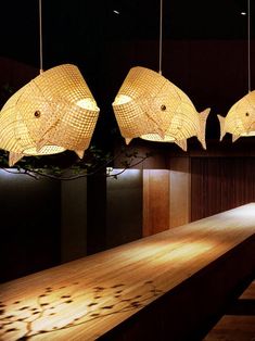 three fish lamps hanging from the ceiling above a wooden table in a room with dark walls