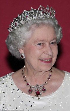 an older woman wearing a tiara and smiling at the camera with red wall behind her