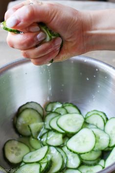 a person is sprinkling cucumbers in a metal bowl