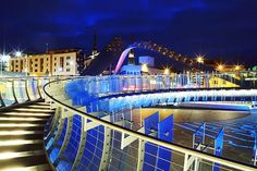 a bridge that is lit up at night with buildings in the background and lights on