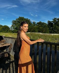 a woman in an orange dress is standing on a deck next to a lake and trees