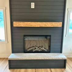 an empty fireplace in a living room with wood flooring and gray painted wall behind it