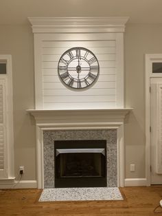 a fireplace with a clock on the mantle above it and shuttered doors in the background